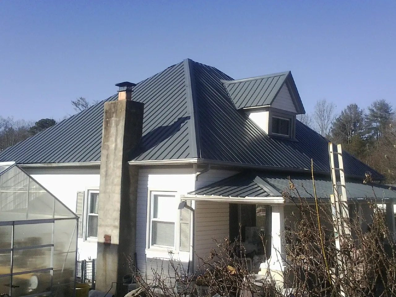 Dark blue standing seam metal roof on a white farmhouse with dormer — Slate & Tile Roof Repair by Roofing Brothers in Spruce Creek