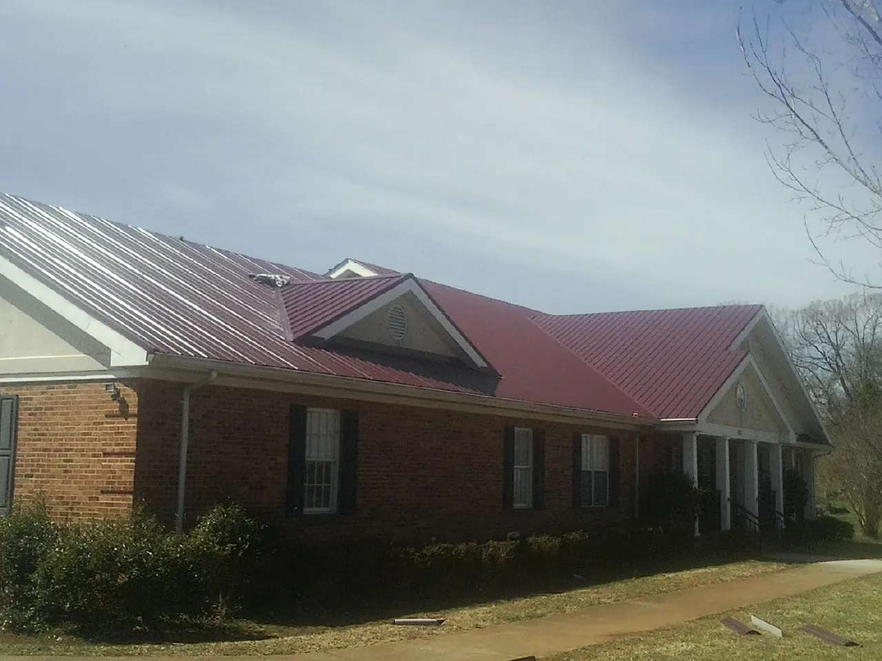 Red metal roof with gabled entries on a long brick building, from a Hail Damage Roof Repair job in Spruce Creek