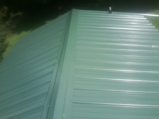 New green metal panels meeting at the ridge of a roof — Flat Roof Repair work by our crew in Spruce Creek