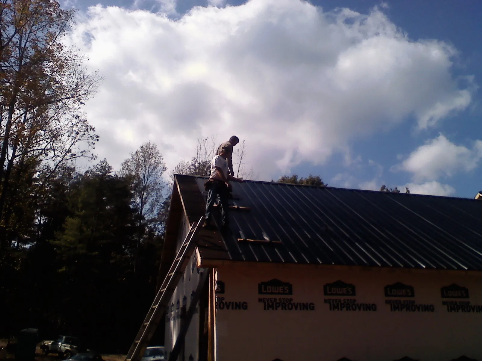Roofer fastening dark metal panels high against a cloudy sky, from a Roof Inspection job in Spruce Creek