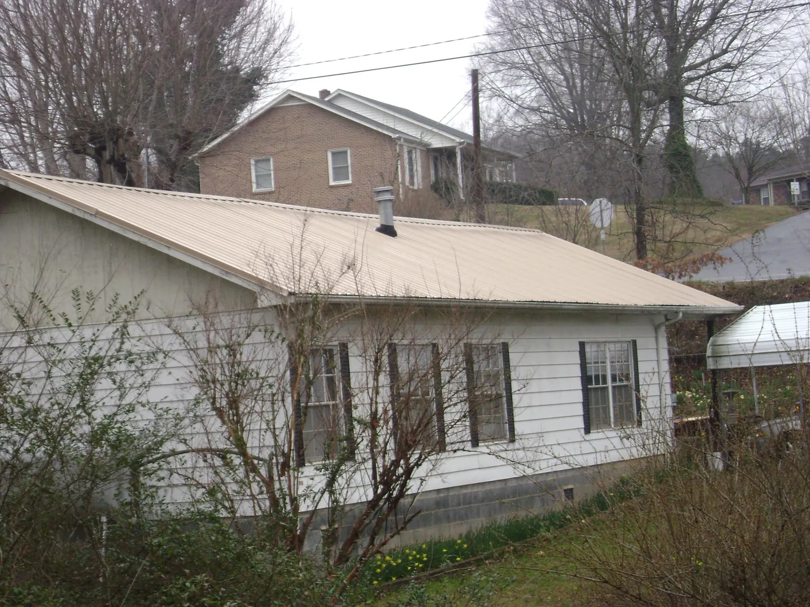 Tan metal roof on a white sided house set into a hillside — Commercial Roofing by Roofing Brothers in Spruce Creek
