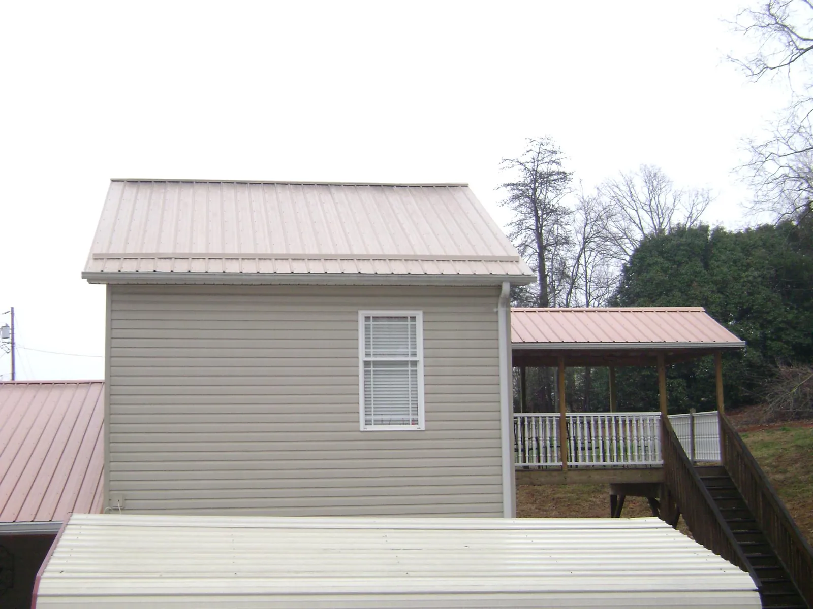 Tan metal roofs on a two story addition and attached porch, from a Roof Replacement job in Spruce Creek